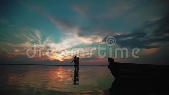慢动作日落时分一个男人沿着水面向一个带着孩子的女人跑来小孩子的剪影视频的预览图