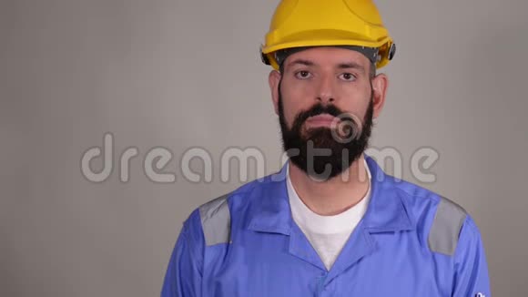 戴着黄色头盔的工人在灰色背景下解释一些事情并表现出良好的姿态视频的预览图