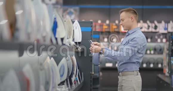 一个年轻的帅哥在一家消费电子商店里选择了一个熨斗作为他的新家研究其特点视频的预览图