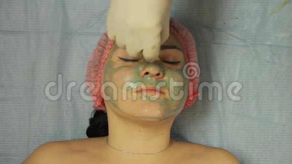 美容师双手戴手套用棉垫从女人脸上摘下泥面膜视频的预览图