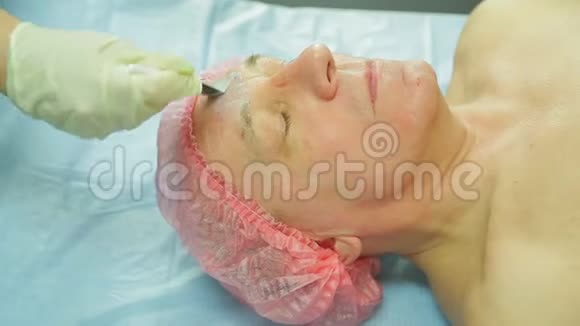 戴手套的女性美容师用刷子把治疗面具涂在男人的脸上侧视图视频的预览图