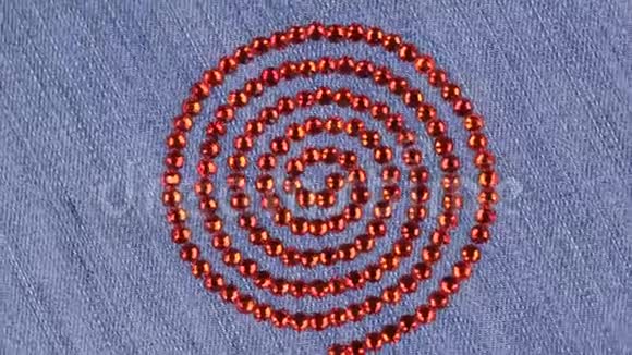 在牛仔布上呈螺旋状排列的莱茵石的旋转上景视频的预览图