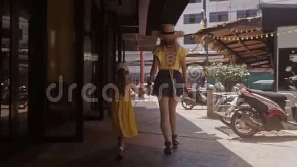 穿着黄色衣服的小女孩和他母亲在街上走到把手前在阳光下热爱家庭生活视频的预览图