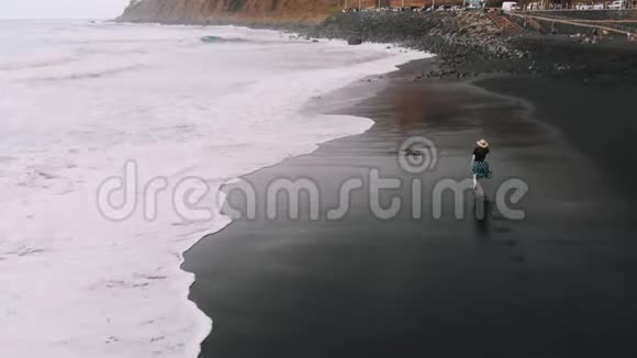 特内里费最佳鸟瞰图穿着时髦的女人在黑色的沙滩上沿着海滩奔跑在她的痕迹后面这就是视频的预览图