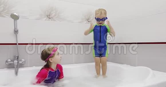 穿着蓝色游泳眼镜的小男孩正在洗澡时在水里跳视频的预览图