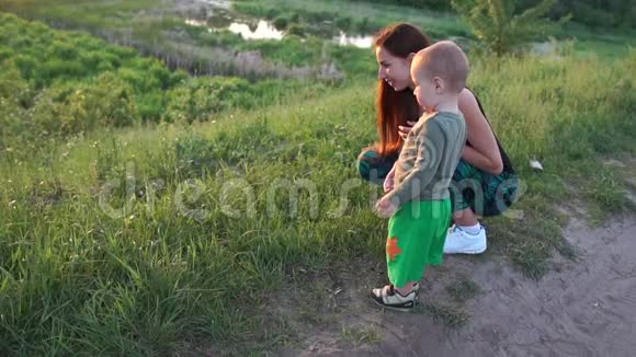 阳光明媚的母亲坐着和她的蹒跚学步的孩子聊天在日落湖在斯洛文尼亚视频的预览图