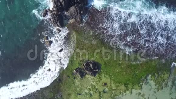 海浪在绿色和棕色的岩石海岸线上翻滚视频的预览图