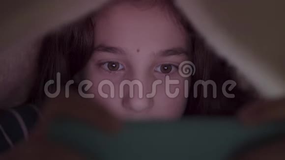 特写肖像可爱的十几岁女孩玩她的手机躺在毯子下特写睡觉时间蓝色的光视频的预览图