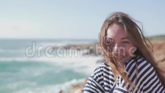 一个年轻的女人坐在岩石上的悬崖上看着大海视频的预览图