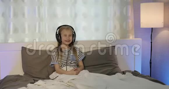 戴着耳机的快乐女孩躺在床上听音乐视频的预览图
