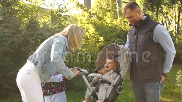 一家人在公园散步妈妈和爸爸带着两个女孩散步坐在婴儿车里的一岁婴儿视频的预览图