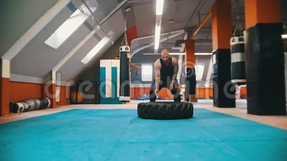 一个纹身很厚的男子健美运动员把轮胎翻在地上在体育馆里用这个动作把它移动起来视频的预览图