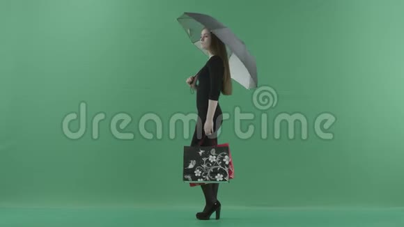 穿着黑色小裙子的漂亮女人正站在一把带购物袋的伞下她站在一边视频的预览图