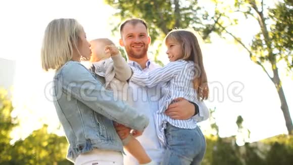 可爱的年轻家庭在公园散步四个人母亲父亲和两个女儿在阳光下视频的预览图