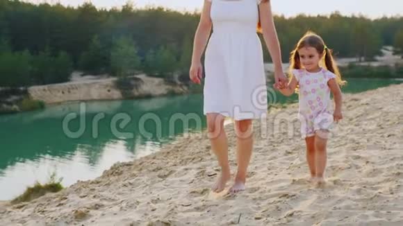 母亲和女儿在美丽的湖水边散步妈妈是一个女孩的手臂视频的预览图