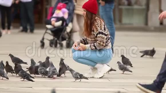 年轻漂亮的女人蹲着喂鸽子在城镇广场的中间视频的预览图