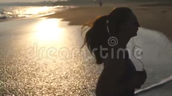 穿着泳衣在海边跑步和听音乐的年轻女子在海边慢跑的女孩剪影女性视频的预览图