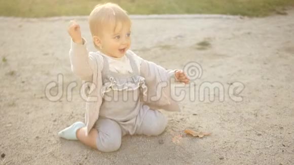 穿着灰色连身裤的可爱女婴坐在沙箱里和沙子在地上玩耍快乐的宝贝视频的预览图