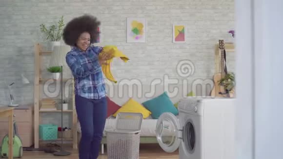 性格开朗富有表现力的非裔美国年轻女性家庭主妇有非洲发型在洗衣机里装衣服洗衣服视频的预览图