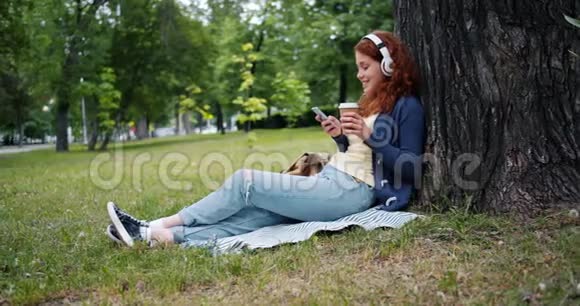 女士耳机享受音乐使用智能手机在公园喝咖啡视频的预览图