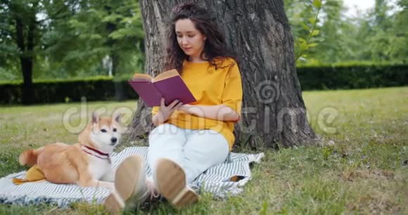 在公园里坐在草坪上带着狗慢悠悠地看书视频的预览图