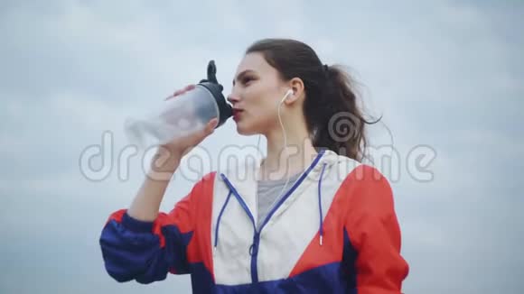 健身妇女跑步后从瓶子里喝水运动女性从健身瓶中饮酒的肖像视频的预览图