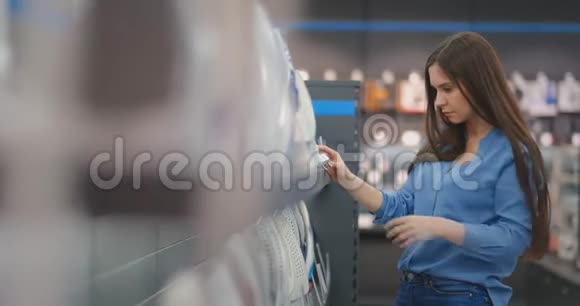 穿着蓝色衬衫和牛仔裤的漂亮性感黑发女人在一家消费电子商店里选择了一个熨斗作为新的选择视频的预览图