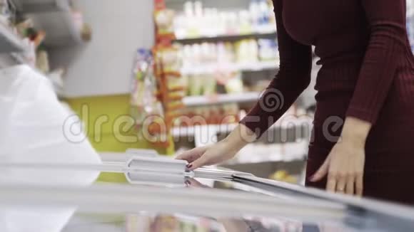 年轻的美女从超市的冰箱里取出冷冻肉视频的预览图