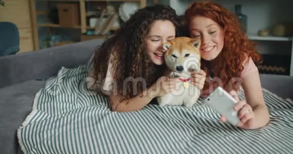 快乐的姐妹们在家里用智能手机和可爱的小狗自拍视频的预览图