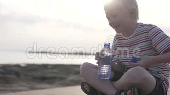 一个孩子在海中日落的背景下喝一瓶水视频的预览图