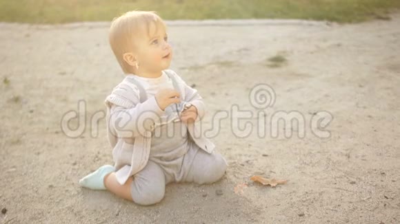 可爱有趣的一岁小女孩坐在沙滩上玩鹅卵石穿着蓝色服装的女孩快乐视频的预览图