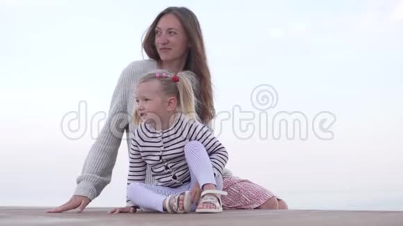 快乐的母亲和她的小女儿在日落时坐在海滩上视频的预览图