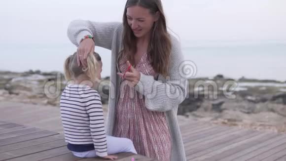 妈妈在海边的海滩上编织一个小女孩的头发视频的预览图