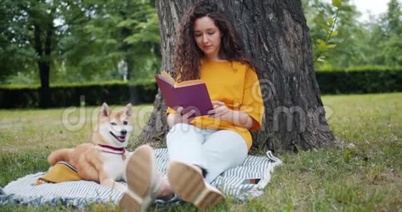 漂亮的卷发女孩和狗坐在公园里看书视频的预览图