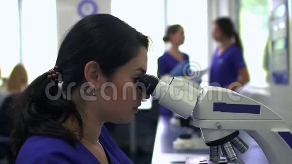 年轻漂亮的女人在实验室用显微镜近距离做分析女士透过显微镜看视频的预览图