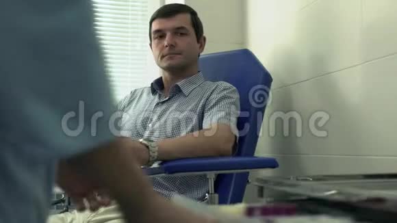 护士的手模糊准备给坐在扶手椅上的成年英俊病人取血视频的预览图