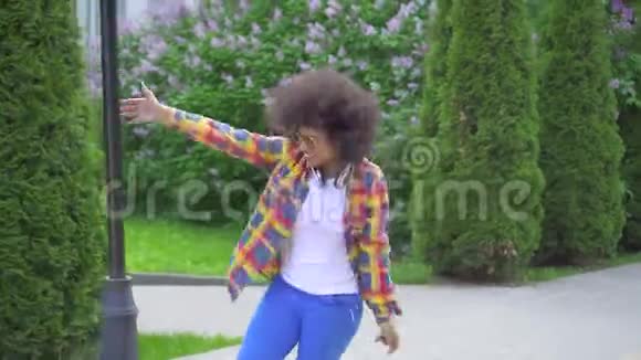 快乐的非洲女人留着非洲发型戴着耳机在街上跳舞唱歌视频的预览图