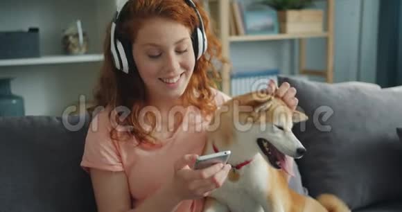 戴着耳机听音乐在沙发上抚摸小狗的美女视频的预览图