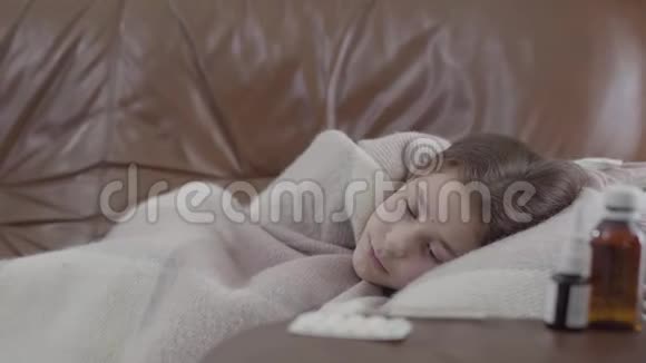 肖像少女生病的女孩躺在沙发上盖着毯子在家里她很冷喷鼻剂药片和糖浆视频的预览图