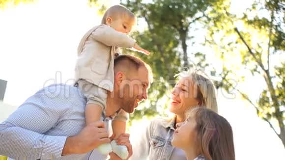 幸福的家庭和两个孩子在阳光下在公园散步父母和两个小女儿视频的预览图