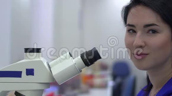 年轻漂亮的女人在实验室用显微镜近距离做分析那位女士微笑着看着镜头视频的预览图