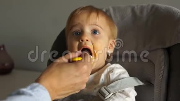 身份不明的母亲用勺子喂她一岁的女儿孩子坐在一张高椅子上健康饮食视频的预览图