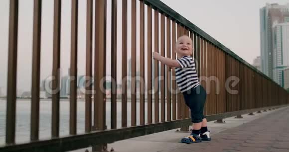 在城市的背景下宝贝可爱的舞蹈牵着手在海滨的栏杆上跳舞视频的预览图