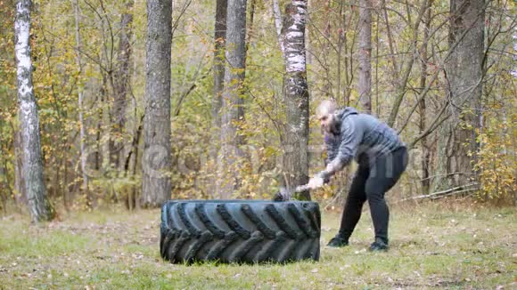 一个强壮的健美男子用金属锤击卡车轮胎秋天的森林视频的预览图