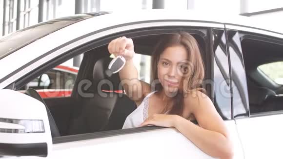 快乐的喜悦黑发的女新车主坐在白色的车上展示了钥匙视频的预览图