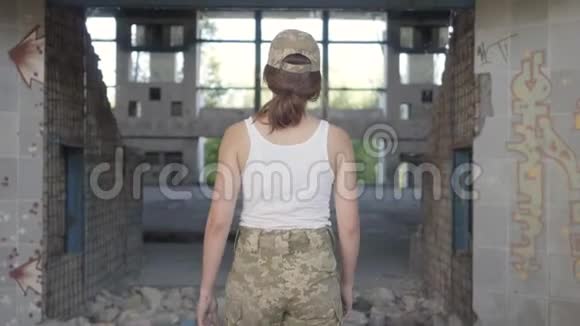 漂亮的年轻女子穿着军装在尘土飞扬的肮脏废弃的建筑里慢慢地走着一个被遗弃的勇士女人视频的预览图