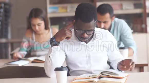 非裔美国男大学生戴着眼镜在图书馆准备考试读着一本书视频的预览图
