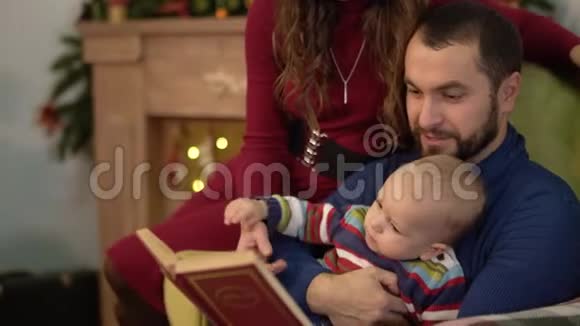 幸福的家庭花时间在一起看书父亲坐在扶手椅上抱着小儿子妈妈视频的预览图