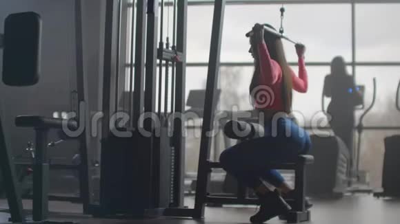 一个年轻的女人正在训练她回到健身房在一个有大窗户的房间里训练一个女人使用视频的预览图