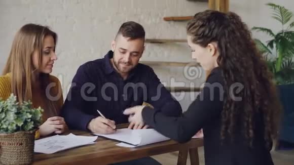 有爱的情侣正在与房产经纪人签订房屋买卖协议在成交后得到钥匙和拥抱视频的预览图